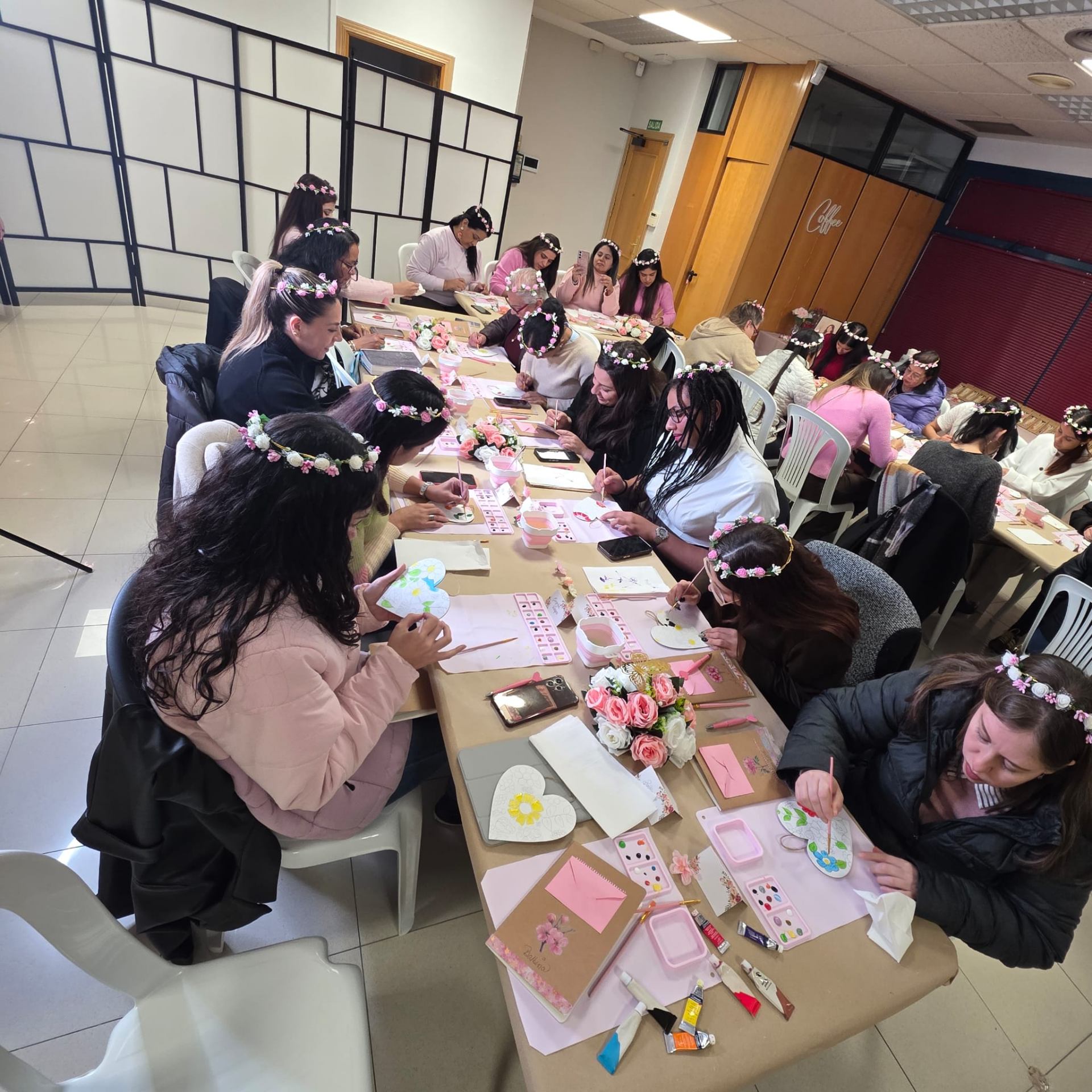Mesa larga con mujeres pintando corazones con coronas de flores